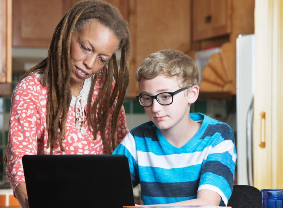 A woman and a boy are looking at a laptop computer.